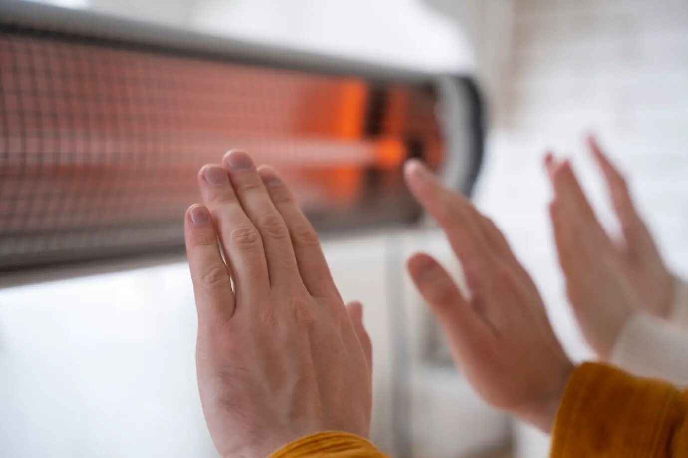 Close-up of people warming their hands near a heater.