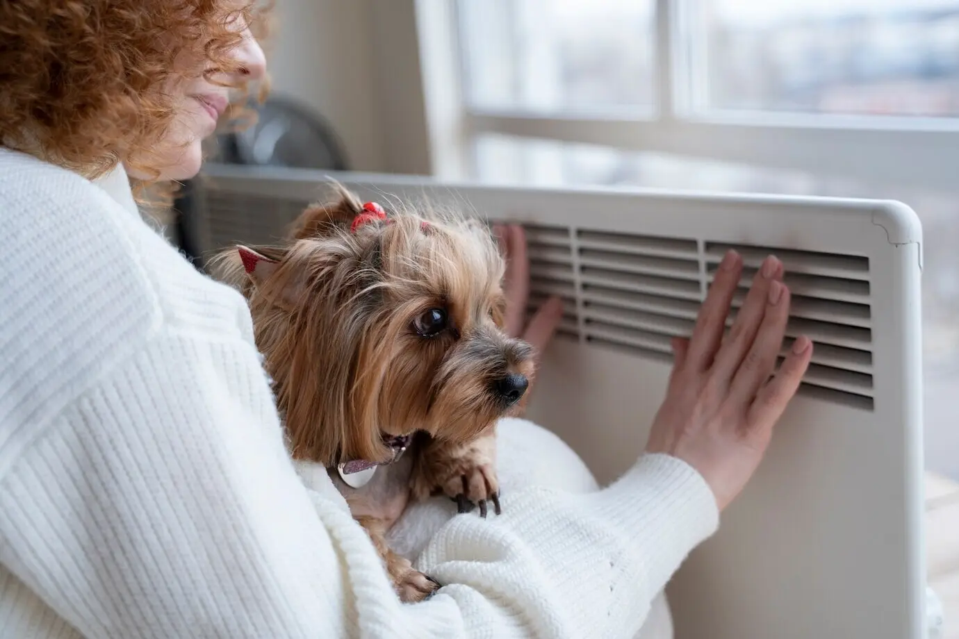 Smiling woman sitting near a heater with a dog